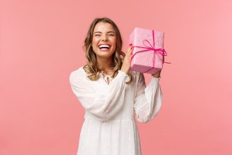 Nasmejana ženska z rožnato zavitim darilom – veselje ob božičnem presenečenju s konopljino kozmetiko ali CBD izdelkom iz Canatura.com.