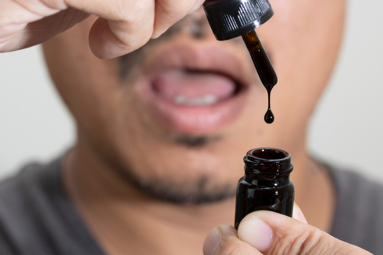 Man using a dropper to place CBD oil from a bottle under his tongue