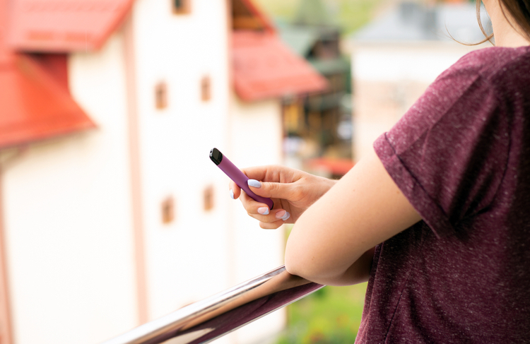 A person holding a purple electronic cigarette while vaping outdoors.
