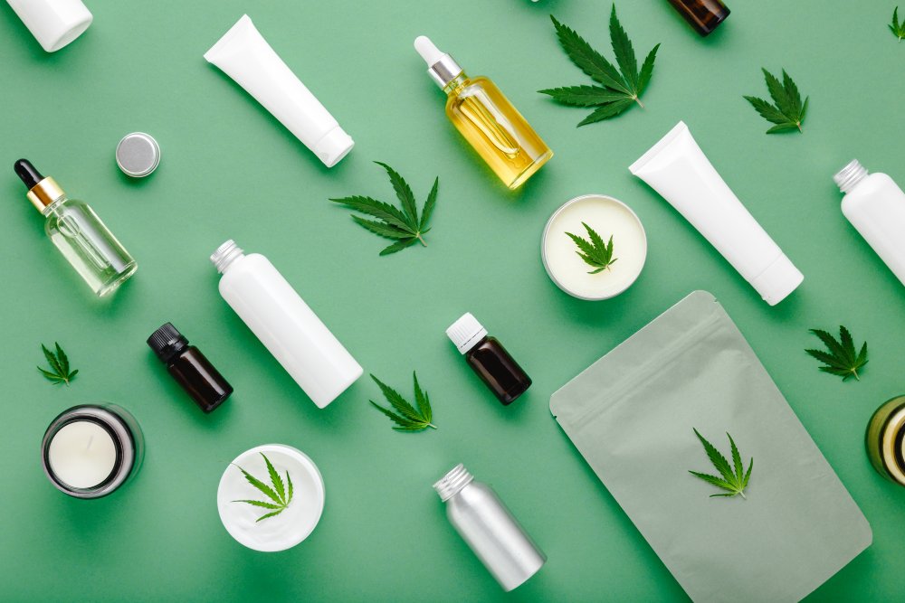 CBD cosmetics – bottles, creams and hemp-based products arranged on a green background with cannabis leaves.