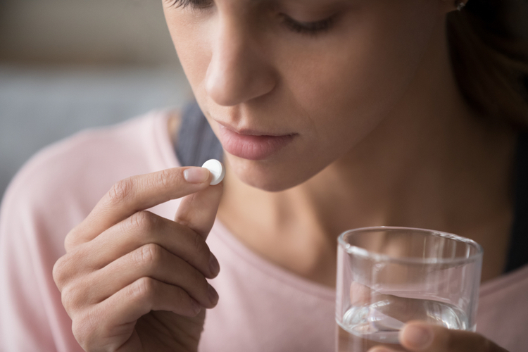 Woman taking a pill with a glass of water – illustrating use of opioid medications for pain relief and related risks