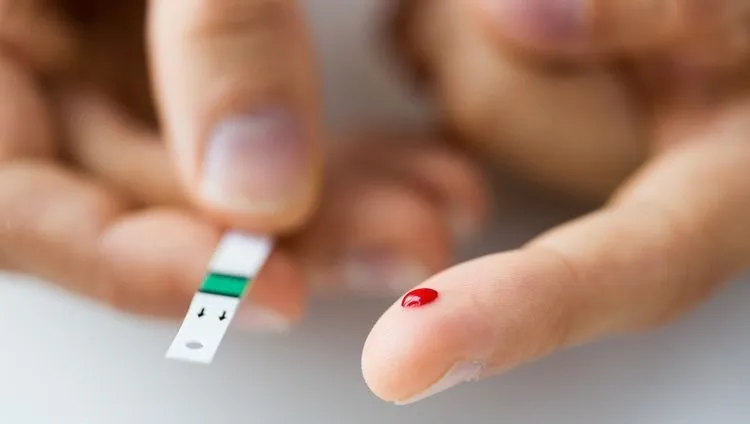 A drop of blood on your finger when measuring blood sugar levels using a test strip – diabetes control