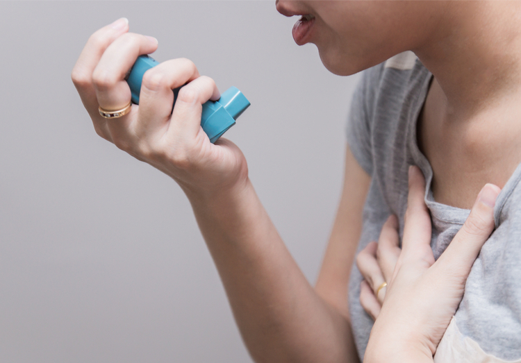 Woman with asthma holding an inhaler to her mouth while clutching her chest