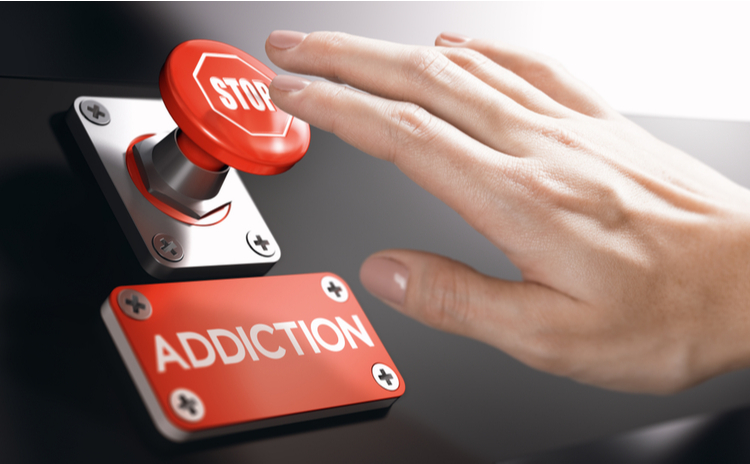 A hand points to the stop button, under which is a metal plate reading: "Addiction"