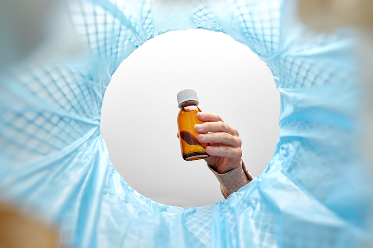 A bottle of CBD oil held by a hand above a basket