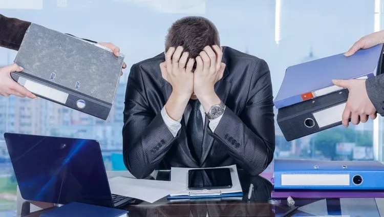 A man in an office is holding his head and is overwhelmed with work tasks – an illustration of burnout syndrome at work