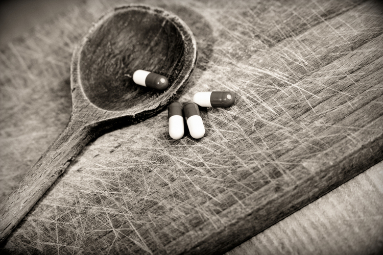 A wooden spoon with capsules placed on it against a gray background