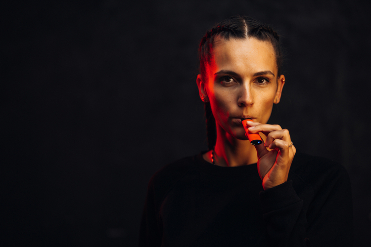 Woman inhaling from a disposable electronic cigarette against a dark background.
